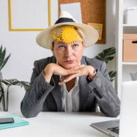 Frau mit Sonnenhut und Sonne auf der Stirn wirkt erschöpft von Hitze im Büro