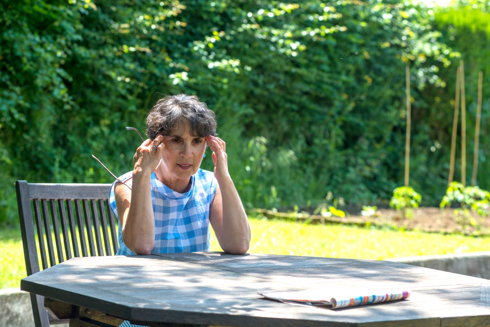 Frau mit Brille in der Hand sitzt am Gartentisch und blickt konzentriert