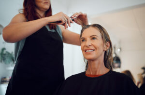 Frau über 50 mit nassen Haaren beim Haareschneiden im Friseursalon