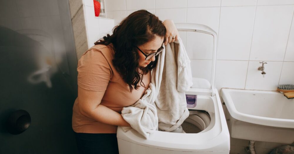 Woman loading a washing machine with laundry indoors. Domestic life in modern laundry room.