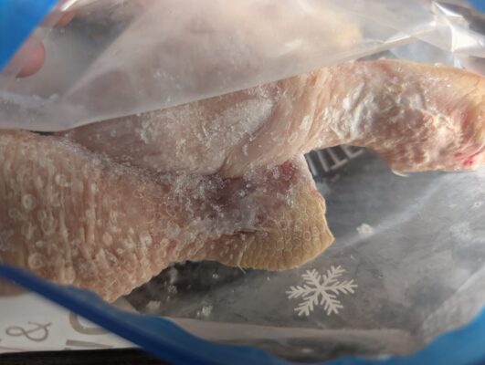 Gefrorenes Hähnchenteil mit deutlichen Gefrierbrand-Stellen in einem Gefrierbeutel.