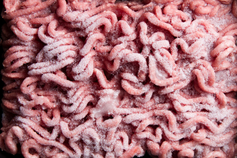 Nahaufnahme von rosa Hackfleisch, dessen einzelne Fleischstränge mit feinen Eiskristallen bedeckt sind.