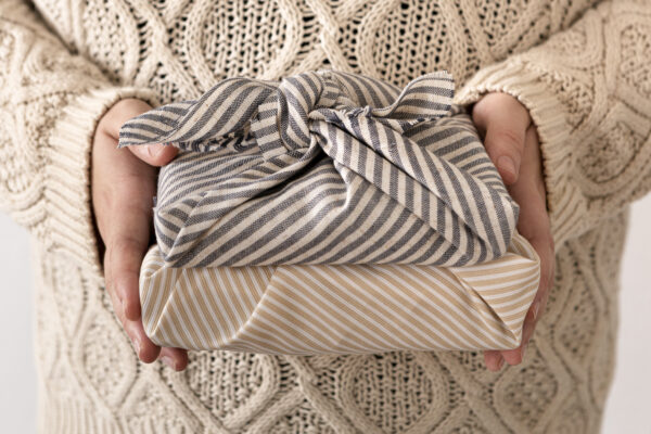 Zwei in gestreifte Stoffe gewickelte Geschenke liegen auf den Händen einer Person vor einem hellen Strickpullover.