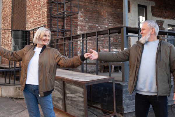 Getrennt leben akzeptieren: erwachsenes Paar hält mit Abstand die Hände, verbunden und lächelnd im urbanen Umfeld.