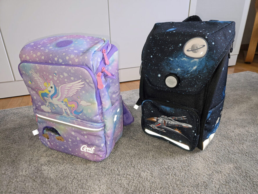 Direkter Vergleich der Schulranzen: Links der GMT LIGHT mit Einhorn-Motiv (Reißverschluss), rechts der formstabile GMT WALL mit Weltraum-Design (Drehverschluss) nebeneinander auf dem Boden.