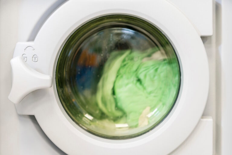 Grüne Wäsche in laufender Waschmaschine, symbolisch für Greenwashing.