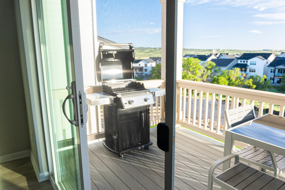 Grillen auf dem Balkon: Blick durch eine Schiebetür auf einen Balkon mit Gasgrill und Sitzmöbeln.
