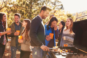 Gruppe junger Menschen lacht beim Grillen im Freien