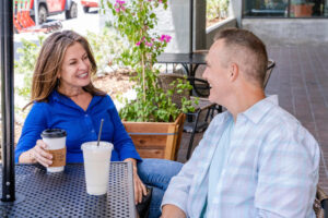 Mann und Frau sitzen entspannt im Straßencafé, trinken Kaffee und unterhalten sich lachend - Symbolbild für gute Fragen zum Kennenlernen und lebendige Gespräche.