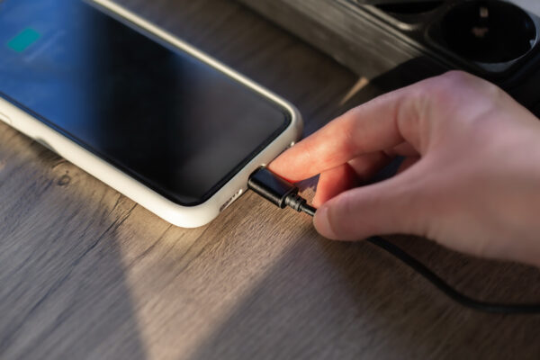 Hand hält ein Ladekabel am Ladeanschluss eines Smartphones
