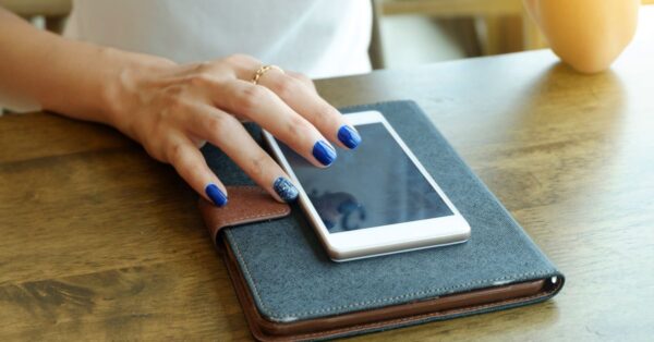 Hand liegt neben einem Smartphone auf einem Tisch, während das Display eingeschaltet ist