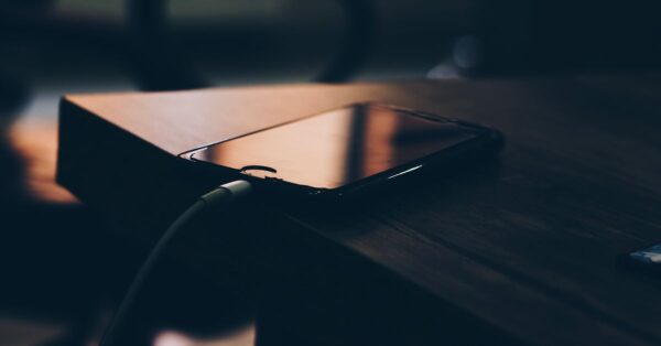 Ein Smartphone liegt beim Laden mit angeschlossenem Kabel auf einem Holztisch.