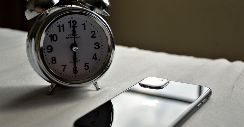 Analoger Wecker und Smartphone liegen nebeneinander auf einem Bett