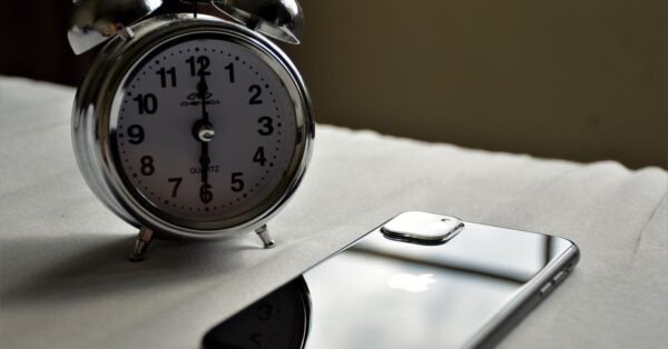 Analoger Wecker und Smartphone liegen nebeneinander auf einem Bett