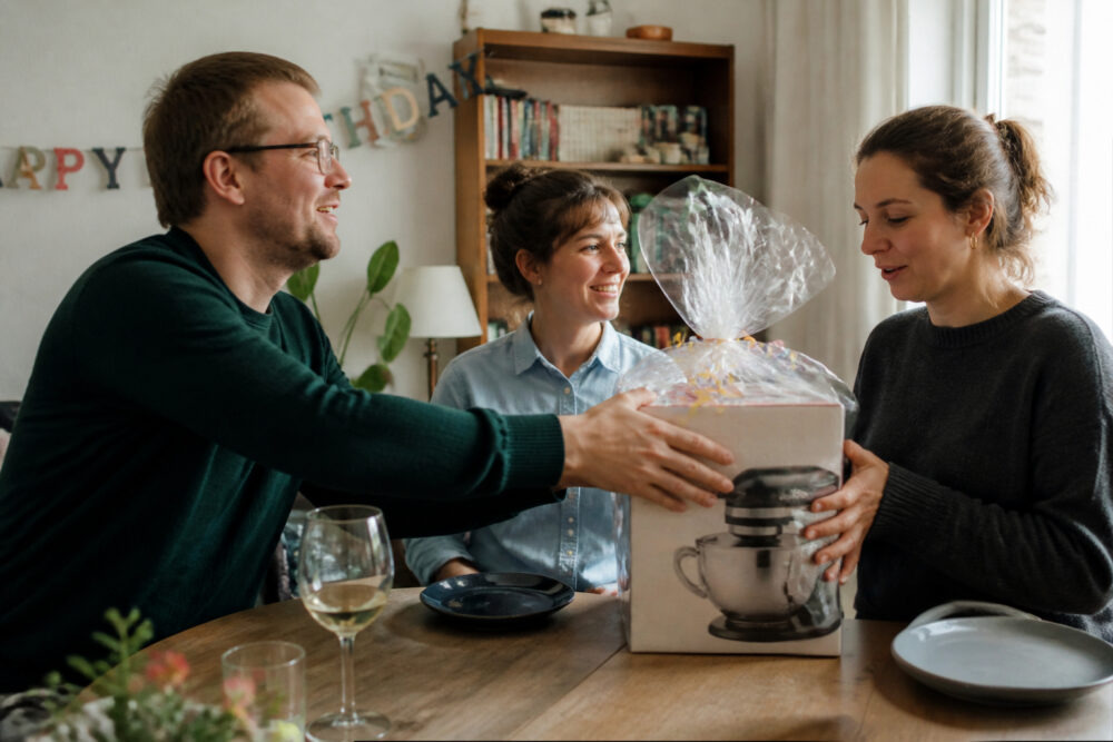 ine Frau bekommt bei einer kleinen Geburtstagsfeier eine verpackte Küchenmaschine als Haushaltsgerät geschenkt.