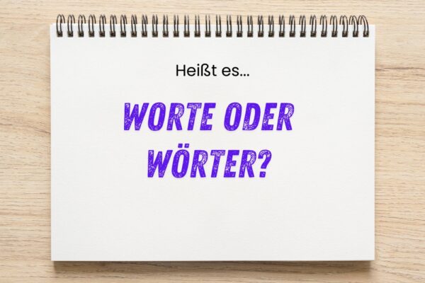 Notizblock mit der Aufschrift „Heißt es… WORTE ODER WÖRTER?“ in schwarzer und lila Schrift auf hellem Holztisch.