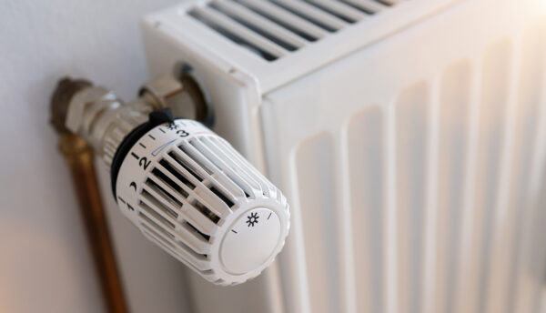 Nahaufnahme eines weißen Heizkörperthermostats an einem weißen Heizkörper mit senkrechten Lamellen.