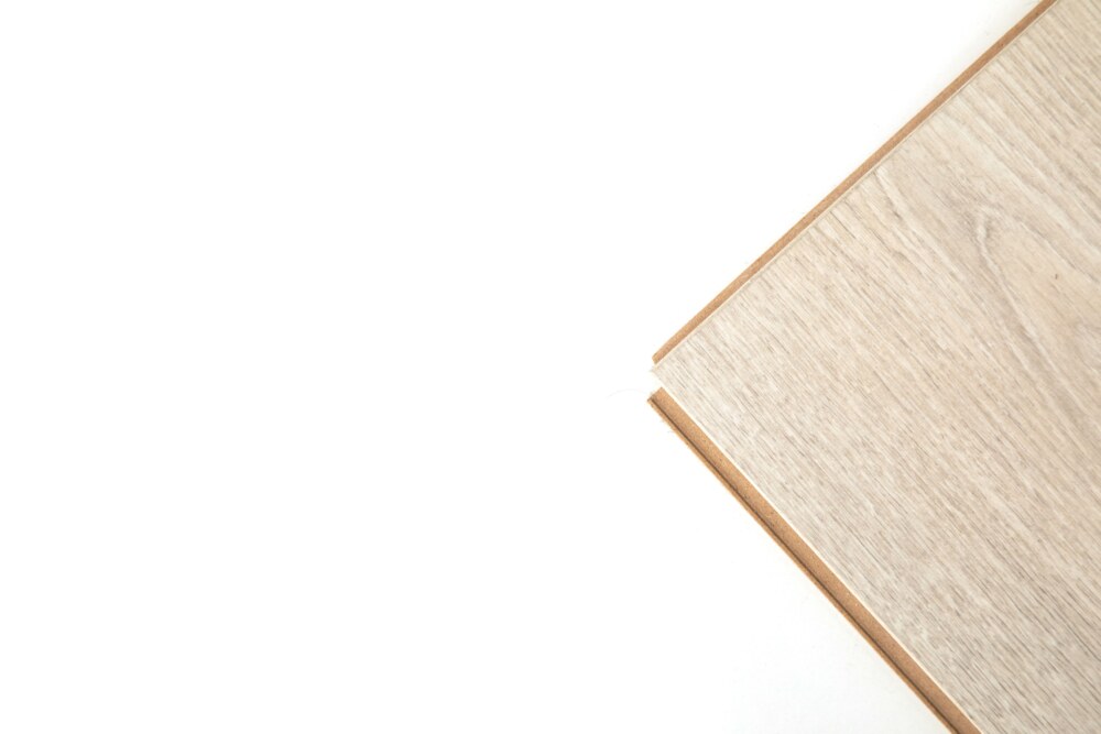 Eine helle, holzgemusterte Laminatdiele liegt schräg auf weißem Hintergrund; ihre Kante ist sichtbar.