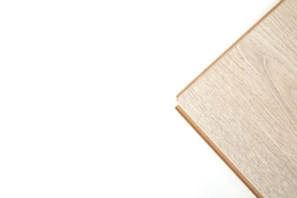 Eine helle, holzgemusterte Laminatdiele liegt schräg auf weißem Hintergrund; ihre Kante ist sichtbar.