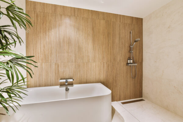 Holzfarbene, senkrecht strukturierte Paneele verkleiden die Wand hinter einer weißen Badewanne und einer Dusche.