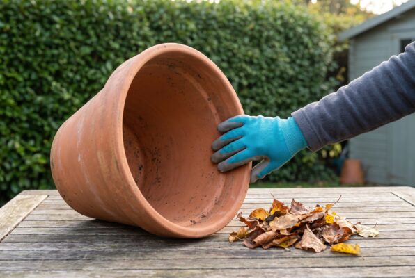 Eine behandschuhte Hand prüft den sich verengenden Innenraum eines seitlich liegenden Terrakotta-Blumentopfs.