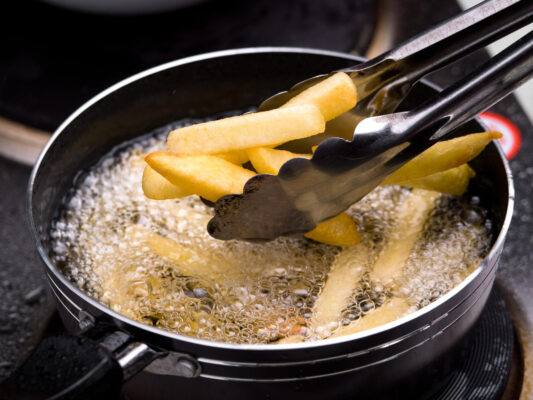 Pommes werden mit einer Zange aus heißem Öl in einer hohen Pfanne gehoben