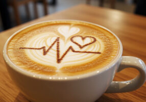Eine Tasse Capucchino mit einer Herzlinie und einem Herz, symbolisch für die Frage, ob Kaffee gesund ist.