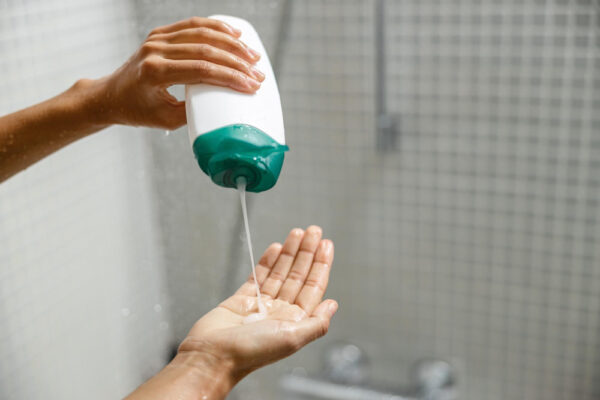 Hand drückt Duschgel aus der Flasche in die Hand unter der Dusche - Ist Duschgel schädlich für die Haare, wenn Shampoo leer ist?