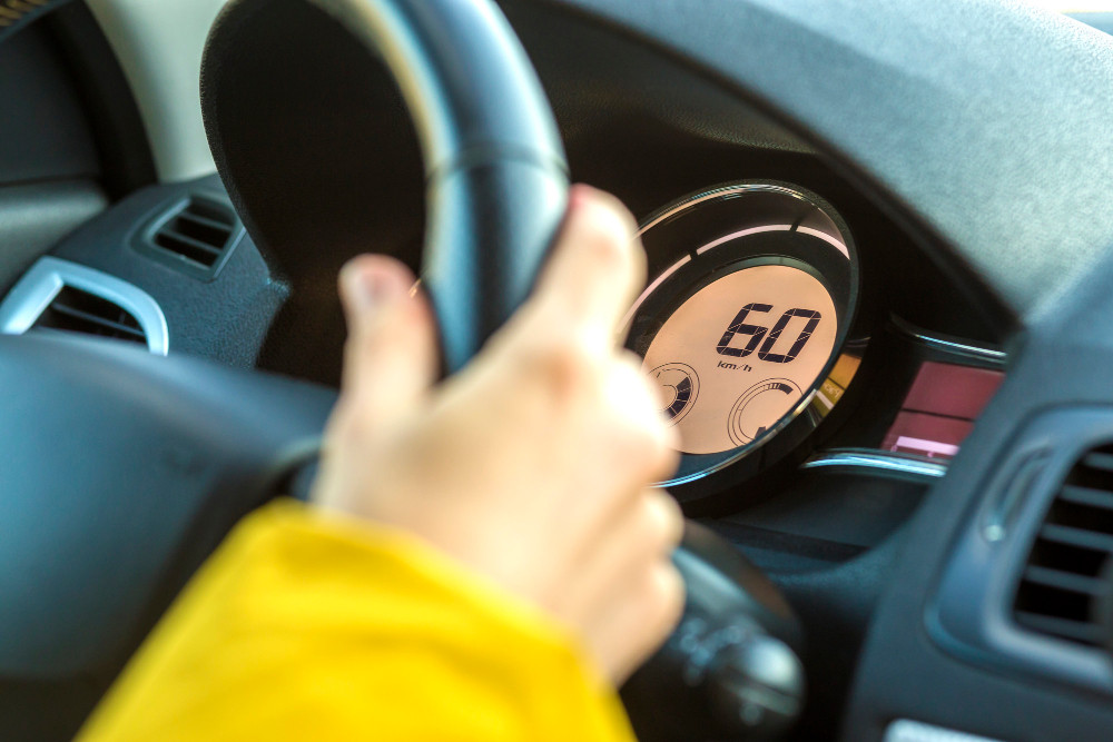 Hand am Lenkrad vor Tacho mit 60 kmh als Symbolbild für langsam fahren im Straßenverkehr