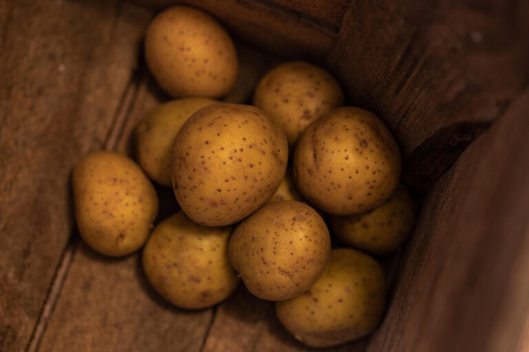 Blick von oben auf einen Vorrat an frischen Kartoffeln, die ideal in einem dunklen, hölzernen Behälter gelagert werden, um sie lange frisch zu halten.