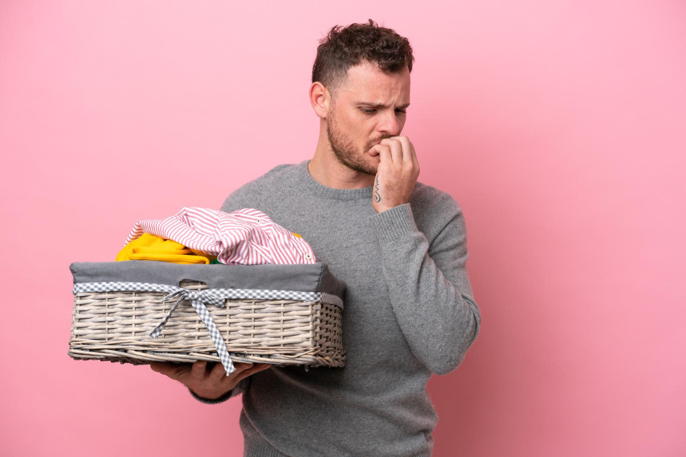 Mann rümpft die Nase über einem Wäschekorb mit Kleidung
