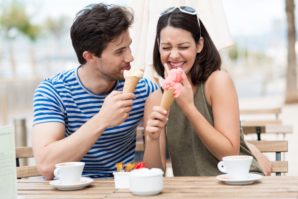 Frau und Mann lachen in der Kennenlernphase beim Eisessen an einem Café-Tisch im Freien