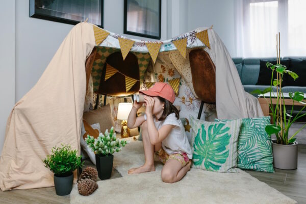 Kind spielt ohne Bildschirm in selbstgebauter Deckenhöhle mit Fernglas im Wohnzimmer, kreative Beschäftigung zuhause