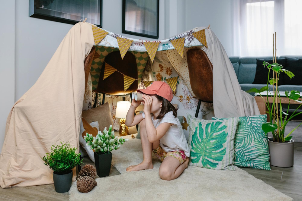 Kind spielt ohne Bildschirm in selbstgebauter Deckenhöhle mit Fernglas im Wohnzimmer, kreative Beschäftigung zuhause