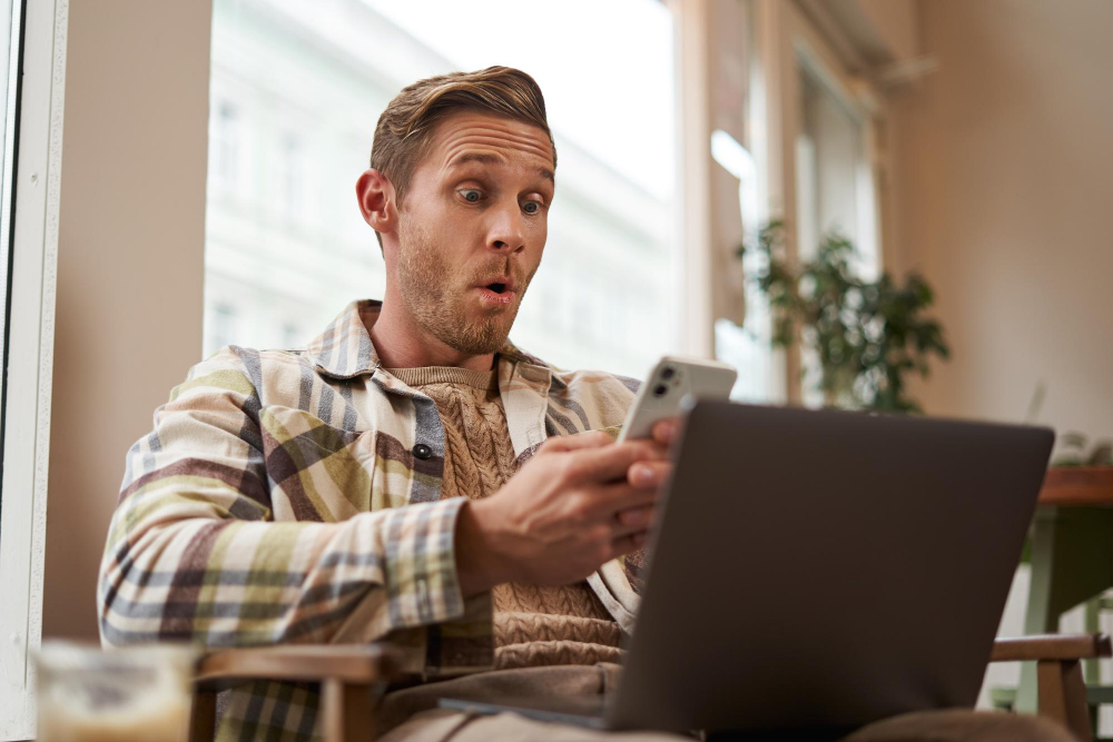 Überraschter Mann zu Hause im Wohnzimmer schaut aufs Smartphone; Kleinanzeigen Betrug erkennen und vermeiden, möglicher Phishing-Hinweis beim Online-Verkauf.