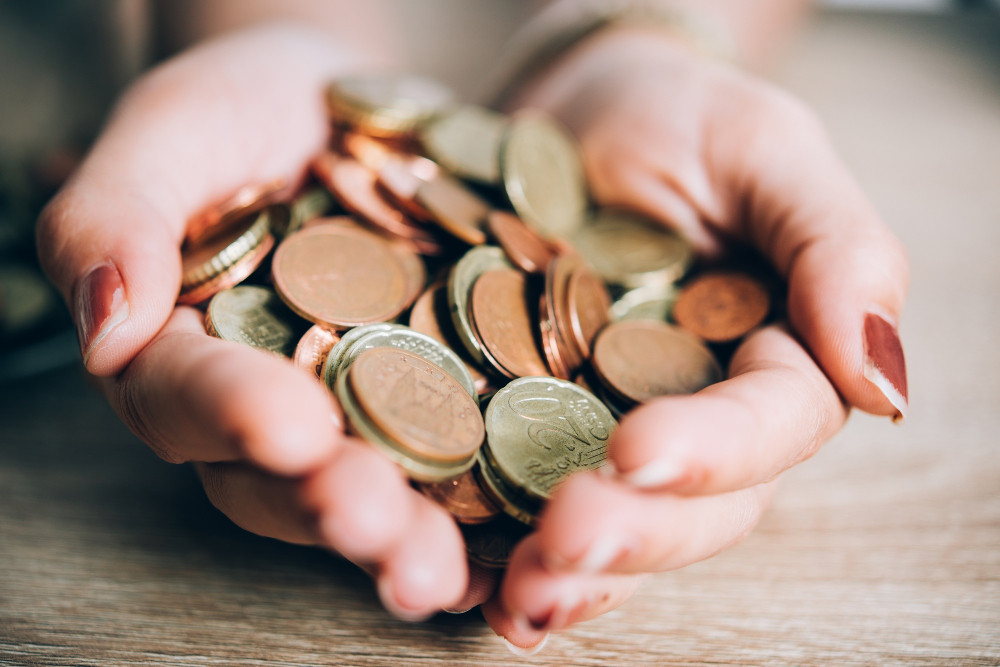 Kleingeld loswerden: Hände halten viele Euro-Münzen, passend zur vollen Spardose und schweren Hosentaschen.