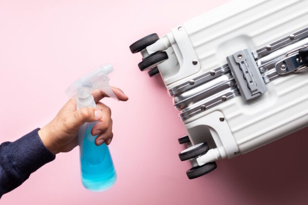 Hand hält Sprühflasche mit Reinigungsmittel neben Koffer