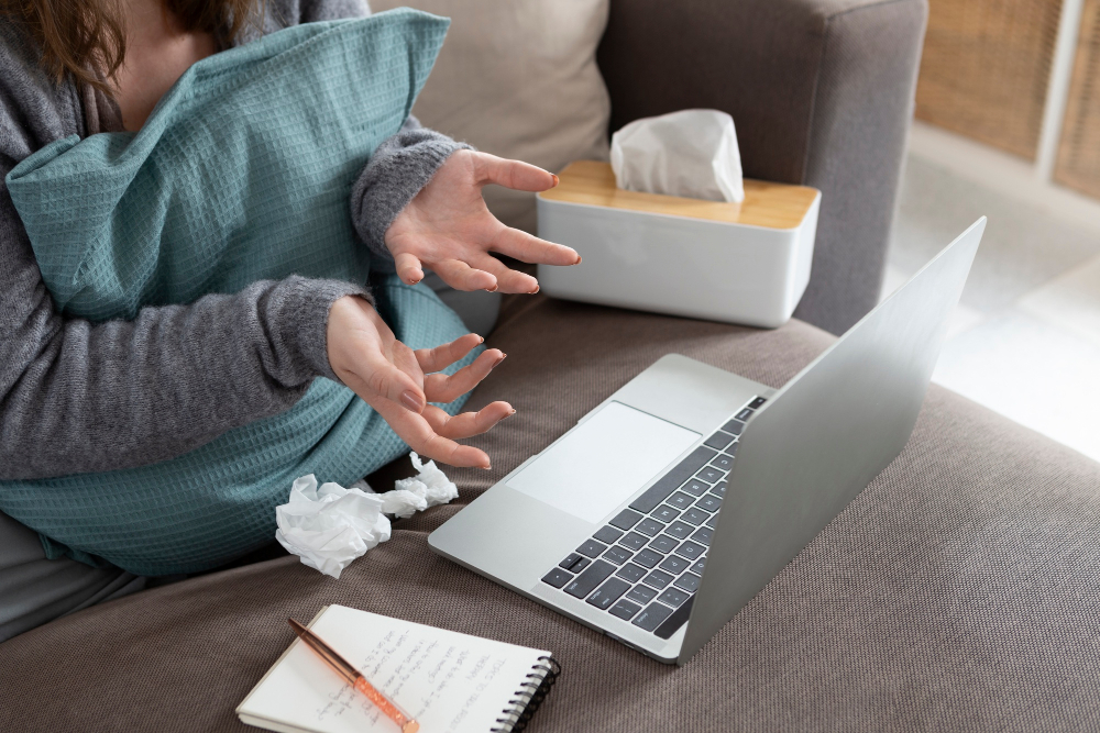 Erkrankte Person mit Laptop, Taschentüchern und Notizbuch auf dem Sofa – Symbol für Krankmeldung per Mail formulieren Beispiele im Arbeitsalltag.