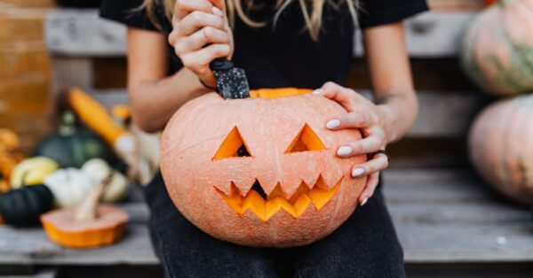 Woman carving a jack-o'-lantern on a bench, perfect for fall celebrations.
