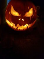 Geschnitzter Halloween-Kürbis mit schrägen Augen, gezacktem Grinsen und warmem Licht von innen