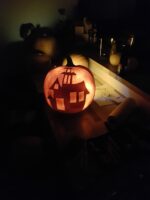 Geschnitzter Halloween-Kürbis mit kleinem Spukhaus-Motiv und leuchtenden Fenstern im Dunkeln