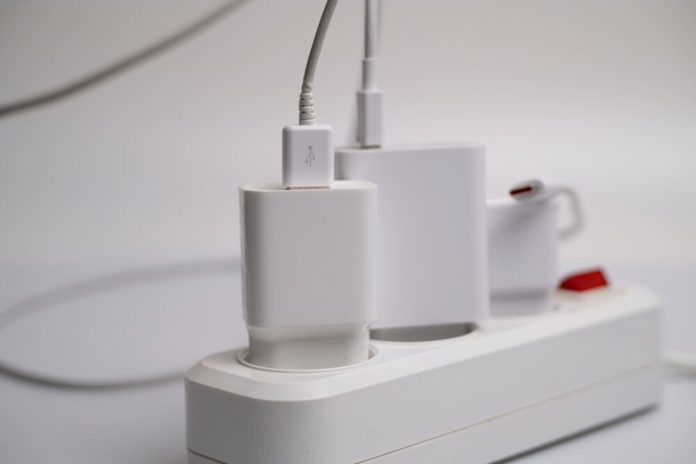 Mehrere weiße Ladegeräte stecken in einer weißen Steckdosenleiste, an einem Adapter hängt ein Kabel.