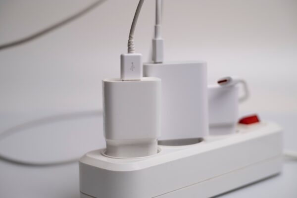 Mehrere weiße Ladegeräte stecken in einer weißen Steckdosenleiste, an einem Adapter hängt ein Kabel.
