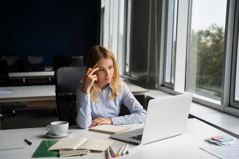 Langeweile auf der Arbeit: Frau sitzt nachdenklich am Schreibtisch vor dem Laptop im Büro.