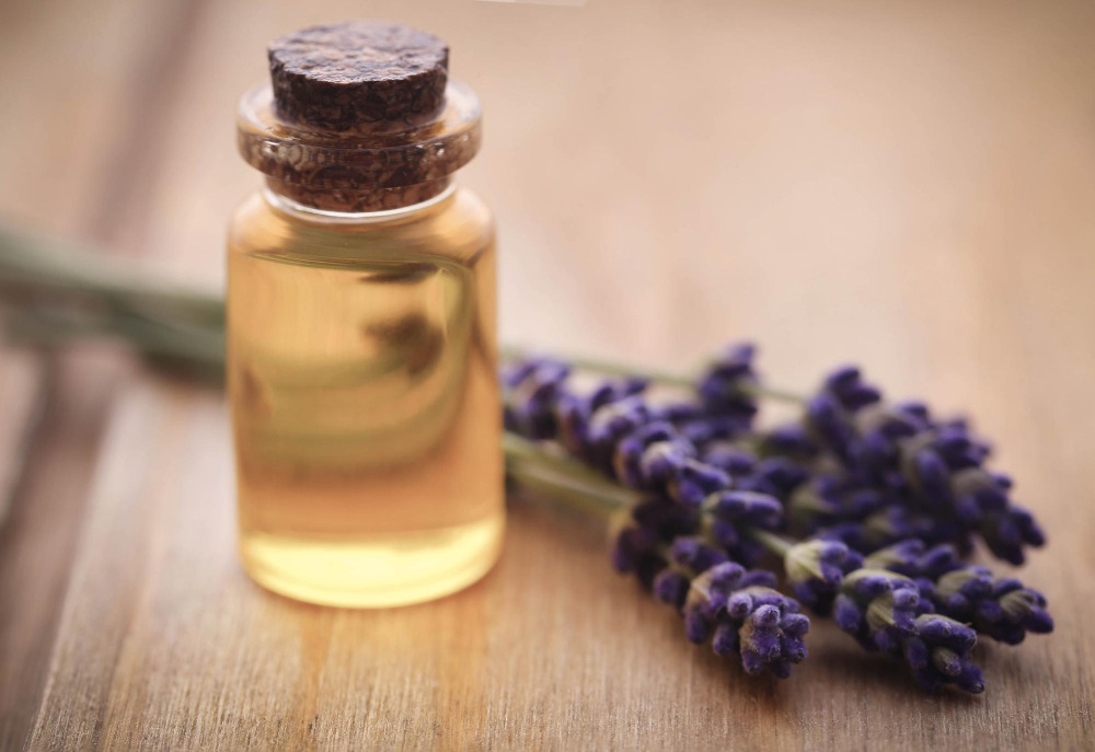 Kleine Glasflasche mit gelblichem Lavendel-Ölauszug neben frischen Lavendelblüten auf einem Holztisch