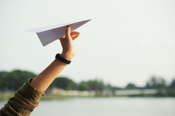 Hand lässt Papierflieger los – Symbol für Loslassen können, Neubeginn und emotionale Leichtigkeit