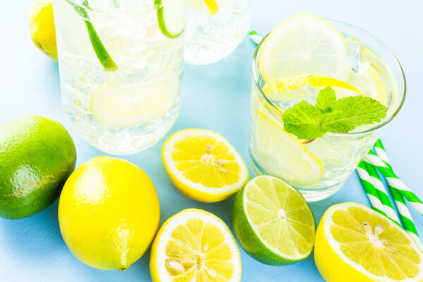 Zitronen, Limetten und Gläser mit Limonade auf heller Fläche