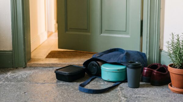 Mehrere Mehrwegboxen und ein Becher stehen neben einer Stofftasche vor der Wohnungstür.