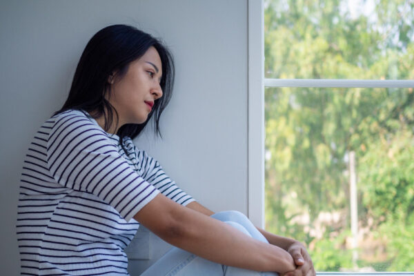 Eine Frau sitzt nachdenklich am Fenster und schaut nach draußen. Das Bild symbolisiert das Thema 'Mein Partner will mich nicht jeden Tag sehen' und drückt die Gefühle von Unsicherheit und Nachdenklichkeit aus, die mit Beziehungsschwierigkeiten verbunden sein können.