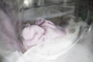 Mikrofaser richtig waschen: rosa Mikrofasertuch im Waschnetz in der Waschmaschine, sanfter Schaum beim Schonwaschgang.